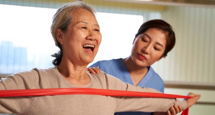 Smiling elderly man seated in a wheelchair with a healthcare professional standing beside him, both looking confident and supported in a clinical setting.