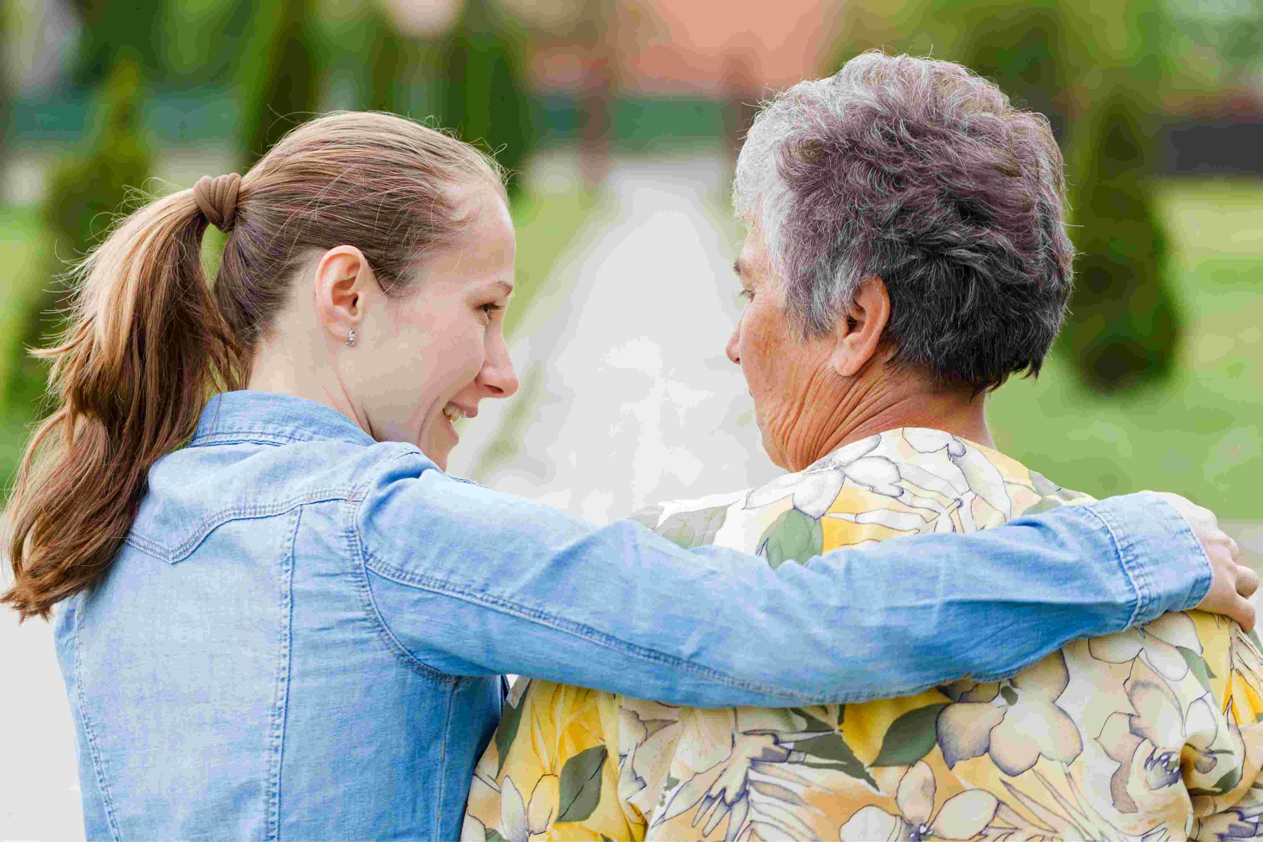 A young woman shares a light moment with an elderly woman outside in the garden, illustrating meaningful companionship and community bonding.
