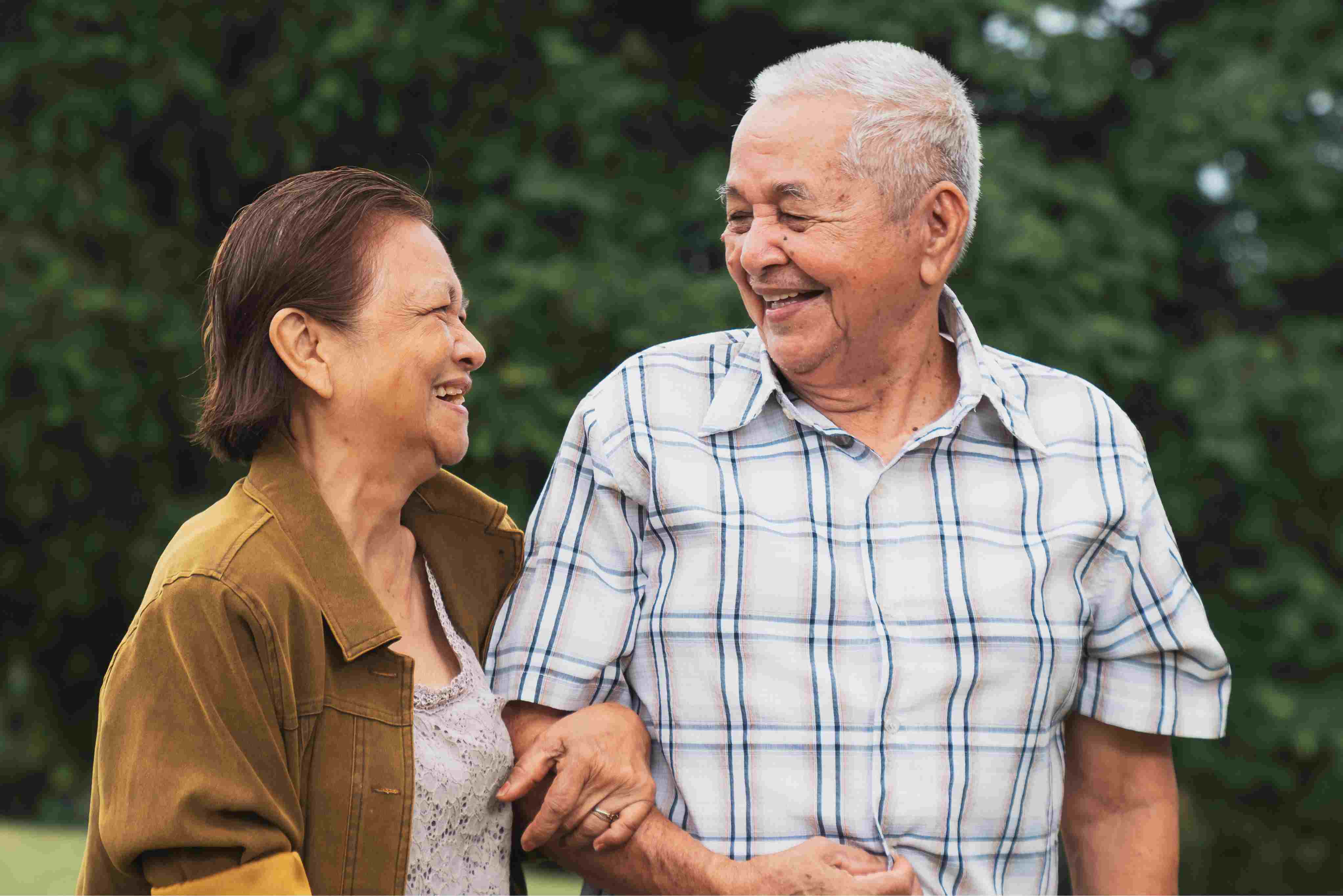 A joyful older couple strolls together, smiling and relaxed, symbolizing independence, connection, and peace of mind in a supportive living environment.