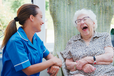 A caregiver and an elderly woman share a joyful moment, laughing together — conveying warmth, companionship, and emotional connection.