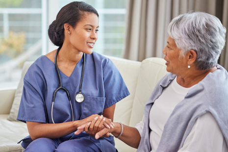 A healthcare professional, wearing scrubs and a stethoscope, holds an elderly woman’s hands in a reassuring way, symbolising trust, empathy, and personalised medical care.